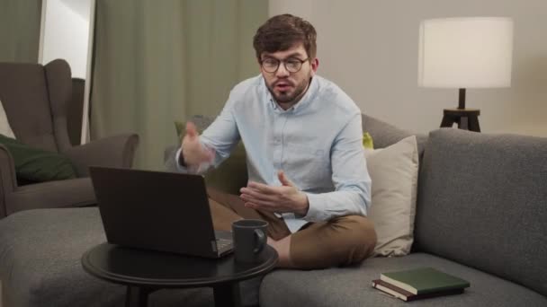 Мужчина в синей рубашке работает из дома с ноутбуком — стоковое видео