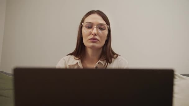 Una chica europea seria habla en un enlace de vídeo en un ordenador. — Vídeos de Stock