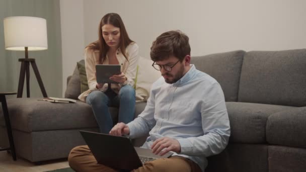 Біла пара чоловік і жінка працюють на ноутбуці, сидячи на дивані — стокове відео
