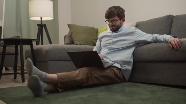 疲れた男が頭を持ち、ノートパソコンを持って床に座って. — ストック動画