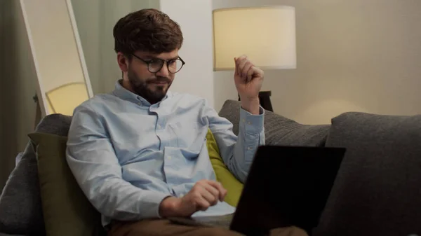 Бородатый белый человек работает на ноутбуке, сидя на диване — стоковое фото