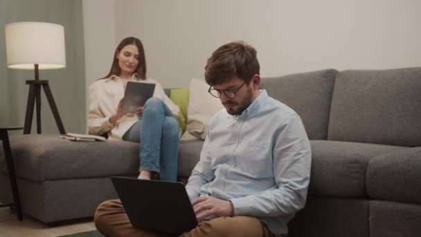 Een Europese man en vrouw op zoek naar gadgets die thuis op de bank zitten. — Stockvideo