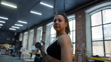 Güçlü bir atletik kadın halterle egzersiz yapıyor ve kameraya bakıyor.