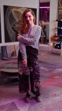 Genç bir sanatçı kameraya poz veriyor ve gülümsüyor. 