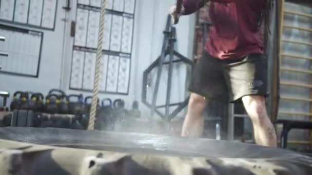 An athletic man is exercising with a sledgehammer and a sports tire — Stock Video