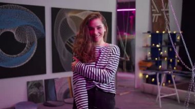 Genç bir sanatçı kameraya poz veriyor ve gülümsüyor. 