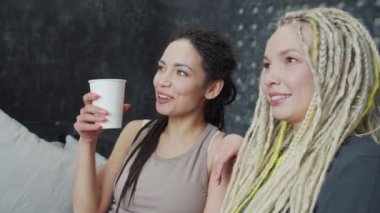 Gülümseyen karizmatik kadın arkadaşıyla konuşuyor ve pencereyi işaret ediyor.