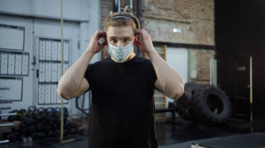 Güçlü bir atlet yüzüne maske takıyor ve kollarını kavuşturuyor.