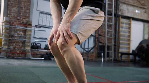 A strong athletic man is limbering up his knee-joints