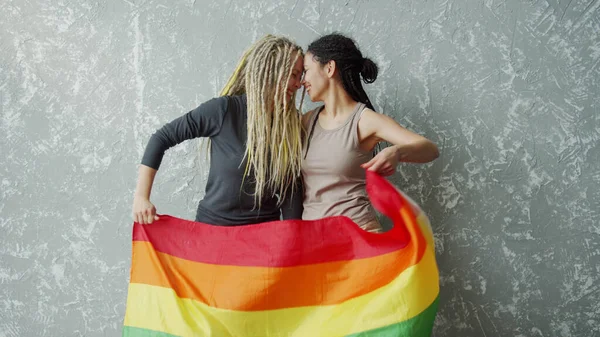 Positieve vriendinnen zwaaien met een LGBTQ vlag en kijken elkaar in de ogen — Stockfoto