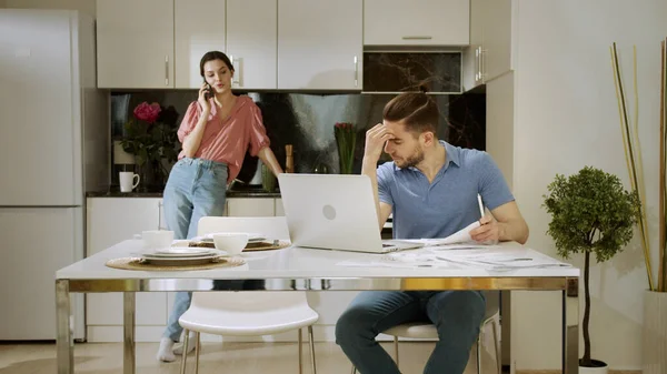 Un hombre serio está trabajando en casa y su esposa está hablando por teléfono y molestándolo. — Foto de Stock