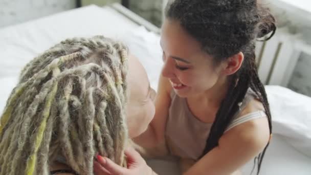 Junge lesbische Frauen sitzen im Bett und berühren sich gegenseitig die Dreadlocks — Stockvideo