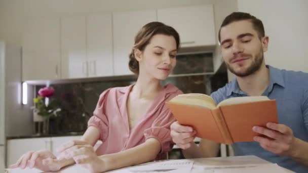 Μια νεαρή κυρία εργάζεται στο σπίτι και ο σύζυγός της κοιτάζει μέσα από το βιβλίο — Αρχείο Βίντεο