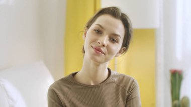 Genç bir kadın kameraya bakıyor ve gülümsüyor.