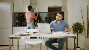 Ciddi bir adam evde çalışıyor ve karısı ona bakıyor ve bir bardak su içiyor.