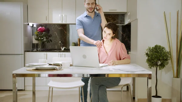 Eine seriöse Frau arbeitet zu Hause und ihr Mann telefoniert und lenkt sie ab — Stockfoto