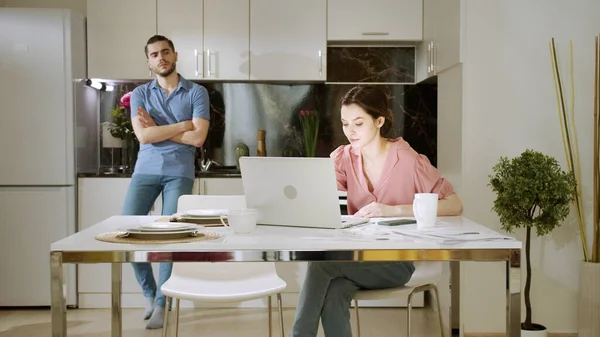 Eine geschäftige Frau arbeitet und telefoniert, während ihr Mann steht und sie ansieht — Stockfoto
