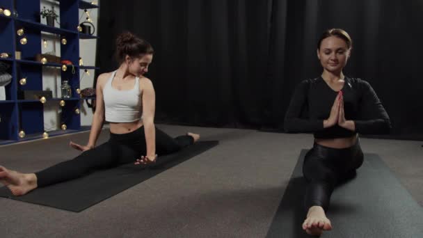 Duas meninas esticar em tapetes escuros em uma sala com cortinas pretas — Vídeo de Stock