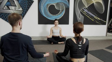 Modern spor kulübündeki insanlarla meditasyon yapan bir kadın.