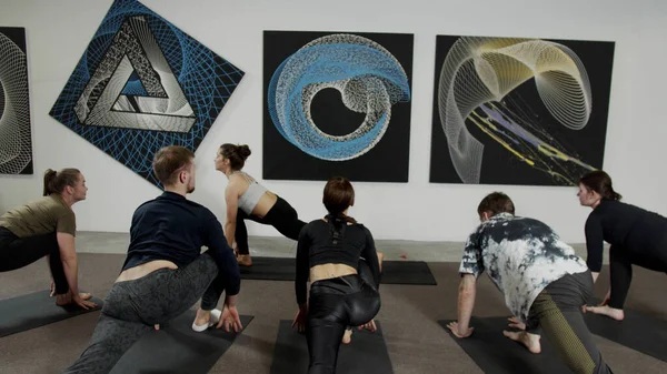 Genç insanlar yoga kursu sırasında karanlık zemini olan küçük bir stüdyoda mümkün olduğunca eğilirler.