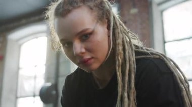 Güçlü bir sporcu kadın kutunun üzerinde oturuyor ve kameraya bakıyor.