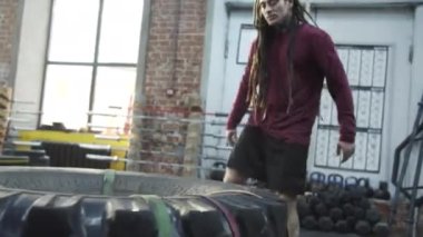An athletic man is jumping on a sports tire