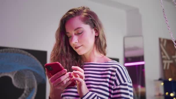 Een aantrekkelijk meisje kijkt naar iets aan de telefoon en glimlacht — Stockvideo