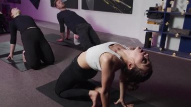 Gençler yoga yapıyor, elleri arkada spor giysiler giyiyor.