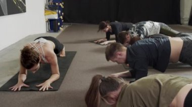 Genç bir kadın takımla yoga yapıyor, spor kıyafetleri giyiyor, siyah pantolonlar ve siyah paspaslar üzerinde bej bluzlar giyiyor.