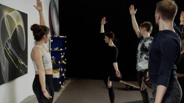 Stüdyoda yoga yaparken tek ayak üstünde duran bir grup zayıf insan.