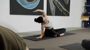 Yoga yapan genç bir kadın, yoga stüdyosunda beyaz bir duvar.