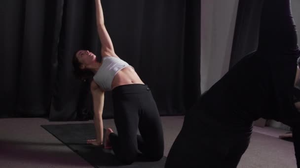 Meisje toont een yoga pose staande op de mat in een licht donkere kamer — Stockvideo