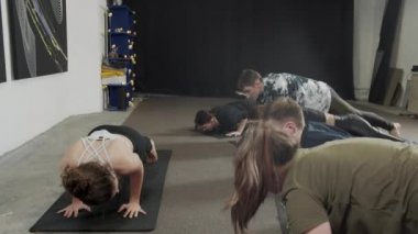 Yoga öğretmeni, genç fitness takımının köpek pozu vermesine yardım ediyor.