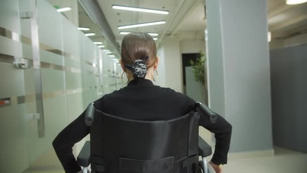 Młoda dama jedzie wózkiem inwalidzkim przez biuro. — Wideo stockowe
