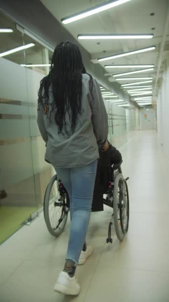 Una giovane donna sta portando il suo collega su una sedia a rotelle attraverso l'ufficio — Video Stock