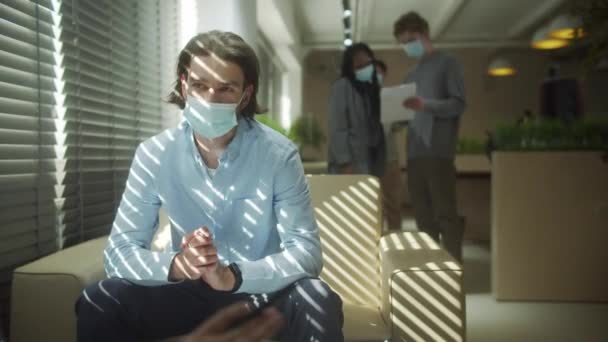 Vážný obchodník sedí v ochranné masce a mluví se svým kolegou — Stock video