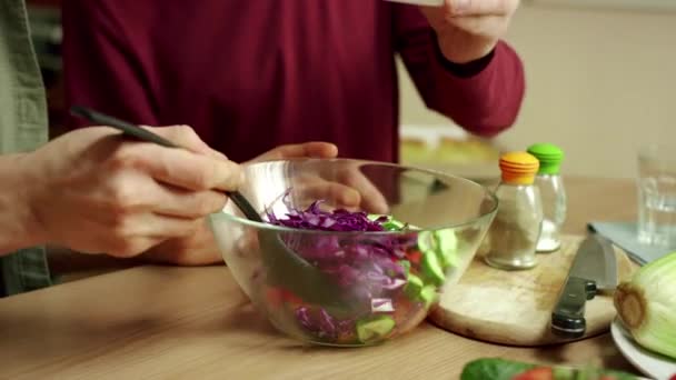 Двоє чоловіків наливають соус на салат і обрізають його — стокове відео