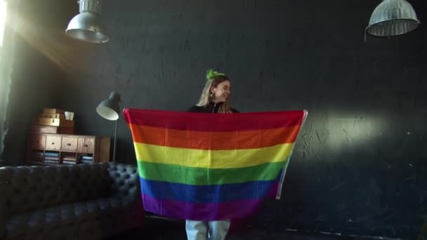 Chica feliz celebra la libertad LGBT y el apoyo con la bandera del arco iris en una habitación oscura — Vídeo de stock
