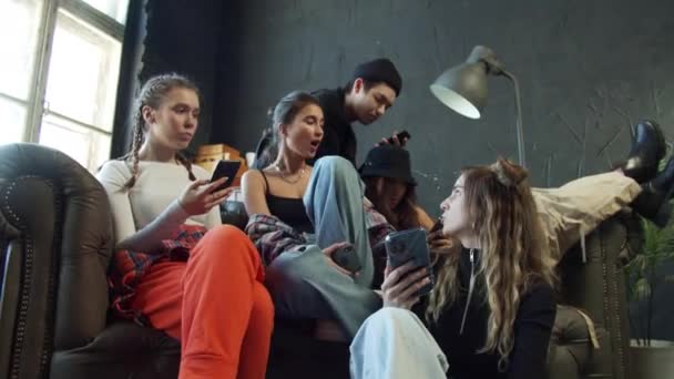 Eine Gruppe junger Leute in modischer Kleidung sitzt auf einer Couch in einem Studio mit dunklem Boden und Hintergrund — Stockvideo