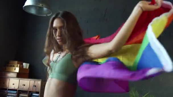 Mladá dívka tančí s duhovou vlajkou LGBTQ ve studiu s černou stěnou a velkým oknem — Stock video