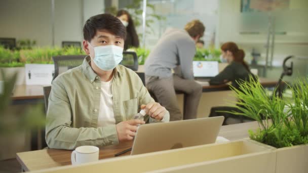 Een jonge collega zit in masker en reinigt zijn handen. — Stockvideo