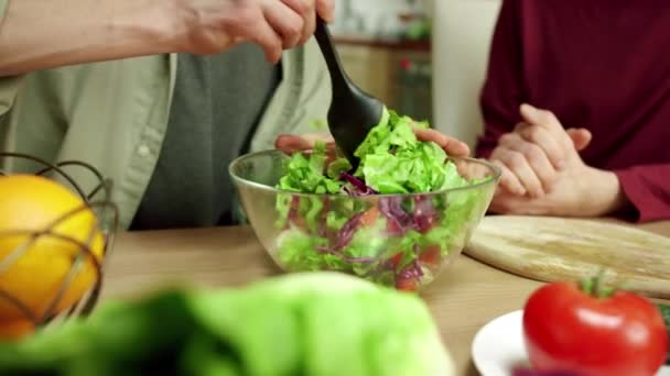 Um homem atraente está misturando a salada e conversando com seu amigo — Vídeo de Stock