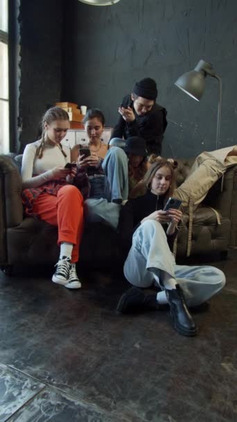 Groep jongeren in modieuze kleding zittend op een bank in een studio met donkere vloer en achtergrond — Stockvideo