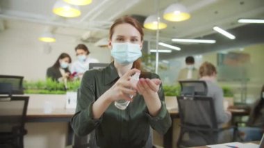 Genç bir bayan ellerini sterilize edip kameraya bakıyor.