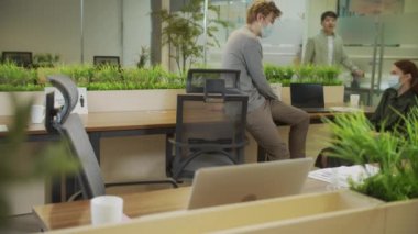 Genç bir adam masasına gidip koruyucu bir maske takıyor. 