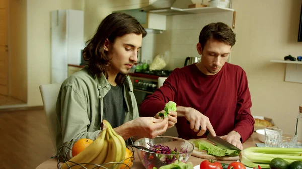 Dos hombres encantadores están cocinando una ensalada juntos — Foto de Stock