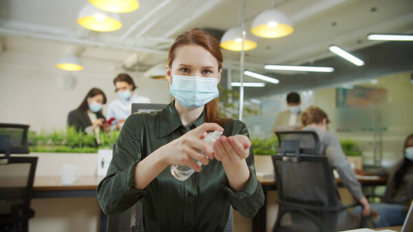 Девушка дезинфицирует руки и смотрит в камеру.