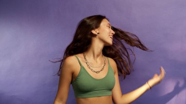 Esmer saçlı genç kız mor bir arka planda dans ediyor.