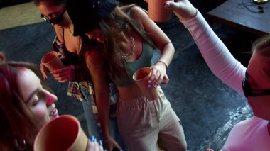 Kulüpte bardaklarda içkilerle dans eden bir grup genç.