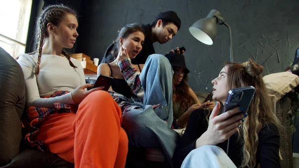 Grupo de jóvenes con ropa de moda sentados en un sofá en un estudio con suelo oscuro y fondo —  Fotos de Stock
